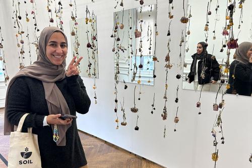 A woman gives a peace sign, standing in front of rows of dried flowers hanging from the ceiling.