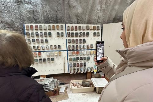 Two women inspect a display board with small hung ceramic tiles, each finished with a different glaze. One woman takes a photo on her cellphone.