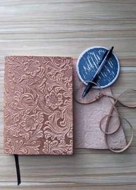 Closeup on a carved leather-bound journal, pen, and blue coaster on a table.