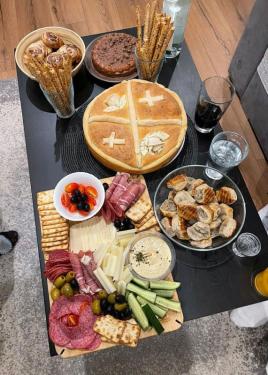 A spread of food on a dining table, including a circular loaf of bread decorated with dough shaped into roses and crosses, breadsticks, and a charcuterie board.