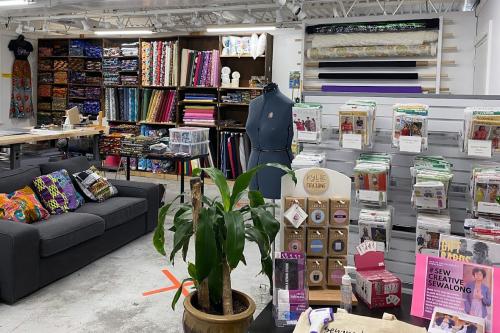 Store interior with racks of fabrics, sewing patterns, and African print pillows on a couch.