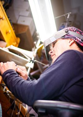 Closer angle of the man in the workshop. Under the magnifying headset, he wears normal glasses.