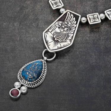 Closeup on a silver necklace with a teardrop-shaped turquoise gem in the middle.