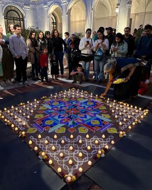 The same scene at night, as the older of the two women courches to place purple and yellow flowers around the edge of their artwork, which is nearly complete with lit electric tea light candles evenly placed throughout the design. A crowd still watches.