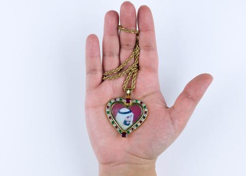 Close-up on a hand, palm facing up to reveal a heart-shaped locket necklace with a portrait of Sheik Zayed.