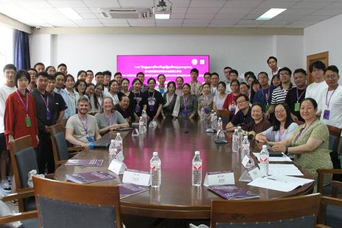 Dozens people pose around a large oval table, all wearing purple badges and lanyards.
