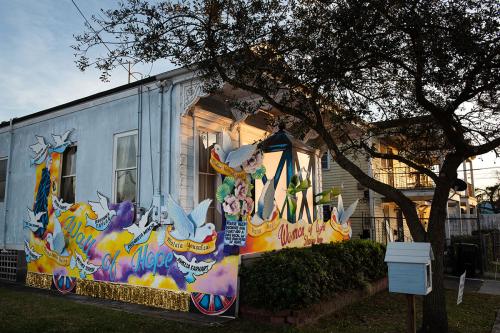 Exterior of a house at dusk, decorated with two-dimensional white doves. Murals read Women Of Light and Wall of Hope, with name of women from history: Mother Teresa, Breonna Taylor, Amelia Earhart, Rosa Parks, and others out of focus.
