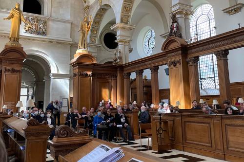 Interior of a church during a service, with people seated in chairs and pews.