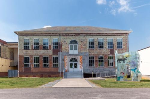 Two-story brick building with a paved walkway, stairway, access ramp, and neat green lawn. To one side of the entrance on the lawn is a large glass sculpture depicting shapes of animals.