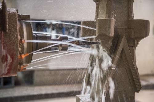 A machine on the left shoots several streams of water at a stone sculpture. In the center of those streams is a drill.