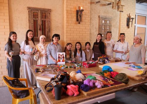 Eleven people pose at a work table set with bundles of dyed wool and felting projects.
