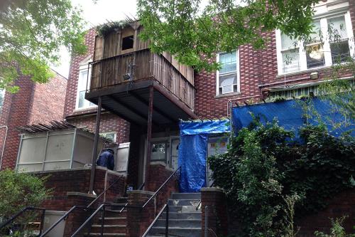 Exterior of a two-story brownstone, with a temporary structure protruding from the upper level, over the entryway.