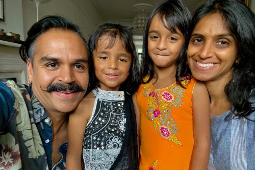 Family selfie, with Sunny Jain (author) on the left with handlebar mustache, gold earring, and blue Hawaiian print shirt. His wife is on the right, with long dark hair and a blue blouse. Their two young daughters are in between, all smiling.