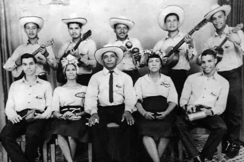 Ten musicians pose, holding their instruments and wearing matching hats and white dress shirts, arranged in two rows. Black-and-white photo.