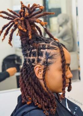 From the side, portrait of a person in a hair salon, their hair styled in dreadlocks, half down and half up in a cylindrical shape like a crown.