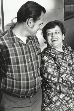 Old black-and-white photo of a couple, looking at each other and laughing. The woman appears to be leaning on the man.