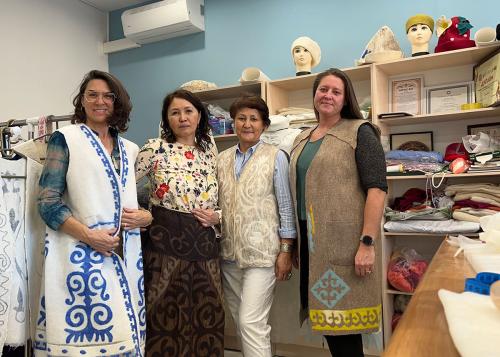 Four women pose in a workshop, each wearing a piece of felted clothing: long sleeveless tunics, skirt, or vest.