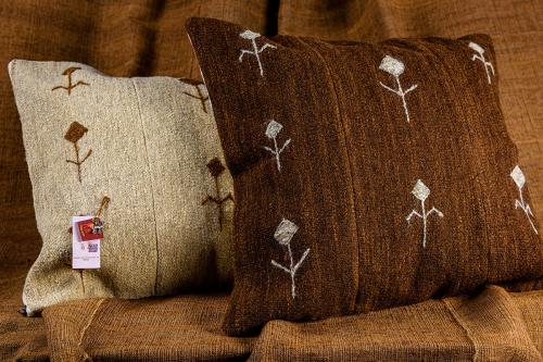 Two square pillows with wool covers in brown and cream, each with a pattern of a human stick figure.