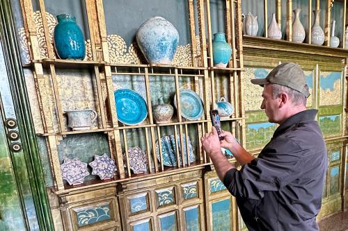 A man takes photos on a cellphone of a gold and turquoise pottery display.