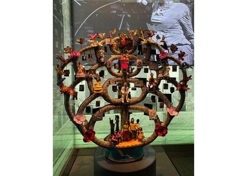 The finished Tree of Life sculpture in a museum display. From this distance, we can see figures of people, flowers, and butterflies.