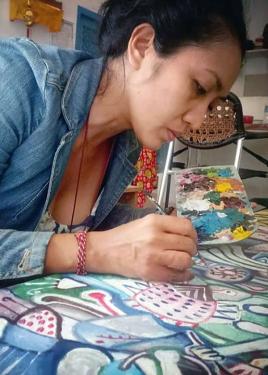 A woman leans over a desk painting on a large canvas.