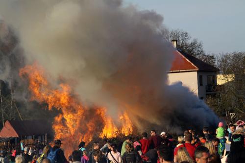 A crowd stands around a burning bonfire and a thick cloud of smoke.