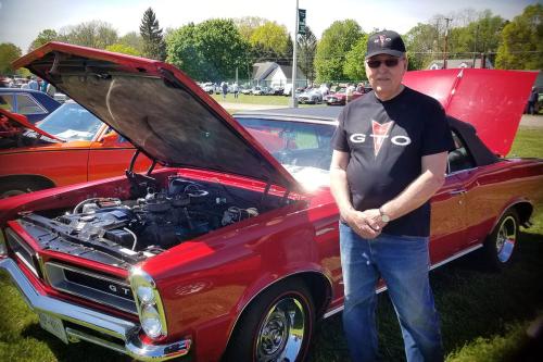 A man poses next to a bright red classic car with the hood and trunk popped open. 