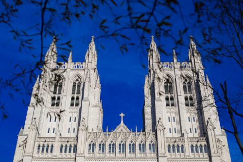 Two white towers of the National Cathedral loom high against a deep blue sky, with thin tree branches silhouetted in black in the foreground.