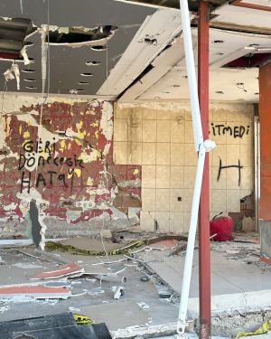 On damaged walls, under crumbling ceilings, black graffiti in Turkish language.