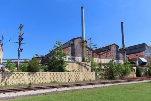 Rusted exterior of a factory, with railroad tracks in the foreground.