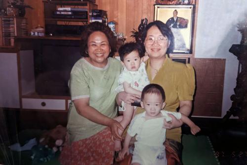 Grandmother, mother, and two young kids posing, smiling, in a living room. Date is stamped in the lower right: 97-5-27.