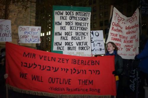 Protest scene with the same red banner with Yiddish text as the first photo. Other signs read: Don't be a patsy, drop the Nazi. How does integrity face oppression?  How does honesty face deception? How does decency fact insult? How does virtue face brute 