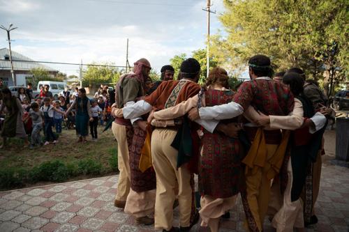 A group of dancers in traditional Armenian dress hold each others shoulders, in a huddle. 