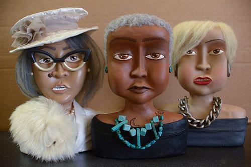 Three Black female dolls each wearing an assortment of accessories. 