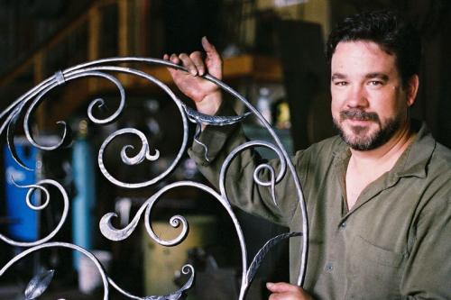 Portrait of a blacksmith holding up a decorative piece of wrought iron.