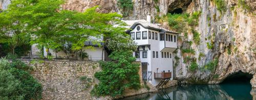 Three-story white building with dark gray trim situated at the edge of a turquoise waterway and the bottom of a sheer rock cliff.