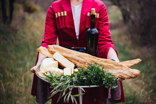 A person, head out of frame, holds a silver platter of breed, cheese, leafy greens, and a wine bottle.