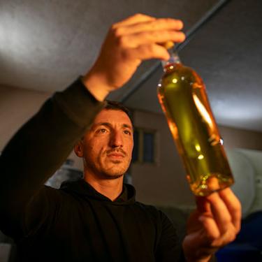 A man holds up a clear bottle of white wine.