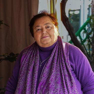 A woman with short hair and purple scarf and sweater smiles faintly.