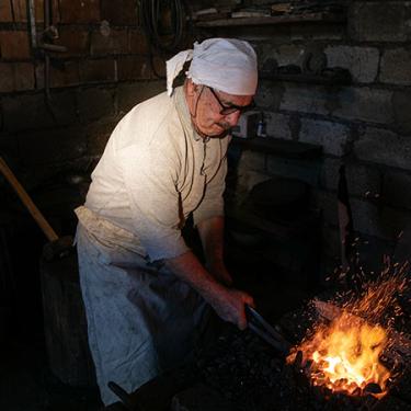 A man holds an object to a fire using a metal tool.