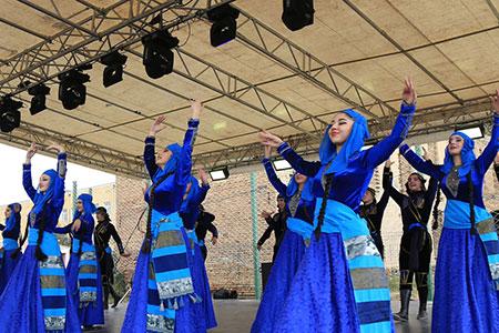 Several adults dance on a stage in loose blue outer garments with their arms lifted in the air.