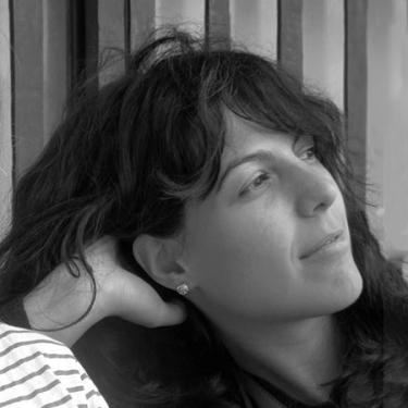 A person with long wavy dark hair leans their head on one hand. Black-and-white photo.