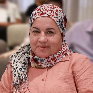 A woman wearing a peach-colored blouse and floral headscarf.