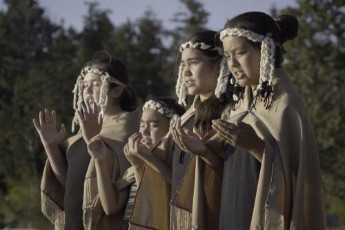 four children in traditional dress with uplifted hands