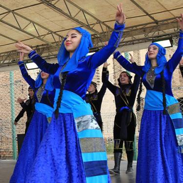 Several adults dance on a stage in loose blue outer garments.