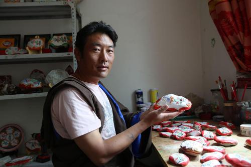 A man holds a stone he carved, painted in white and red.