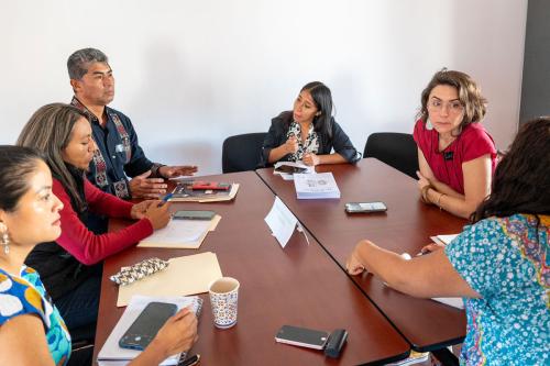 Six people sit around a table talking.