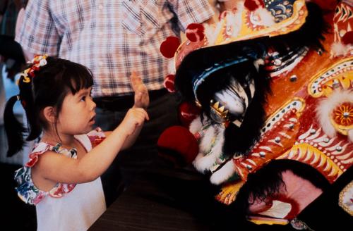A young girl holds her hands up to a large lion dance puppet.