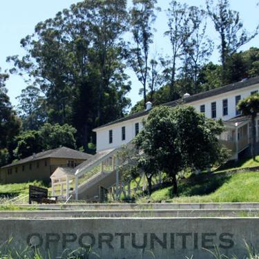 Exterior of a large two-story building from further down a hill. Carved concrete stair in front reads OPPORTUNITIES.
