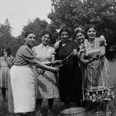 Captured in black and white, a group of women stands together smiling. They hold kabobs and other traditional Armenian food they have prepared for a picnic.